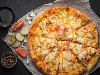 Delicious traditional homemade pizza with tomato, pepper, sausage, cheese on a black background.