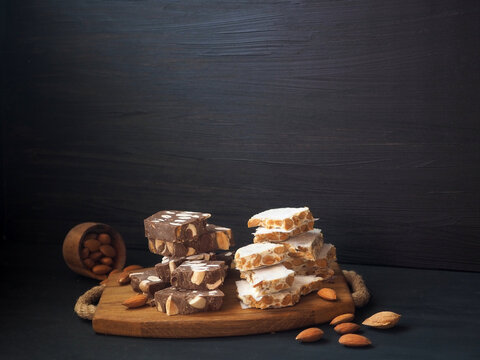 Traditional Spanish turron with almonds on a wooden board. On a black background