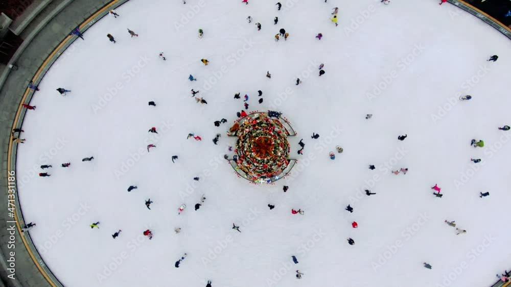 Wall mural Top view of many people skate on ice rink around Christmas tree in park on winter holidays. Active healthy lifestyle entertainment for family and kids outdoor. Ice Skating. High quality 4k footage