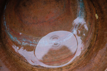 Water in a copper pot in the rain. The blue circle of oxidized copper. 