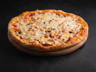 Delicious traditional homemade pizza with tomato, pepper, sausage, cheese on a black background.