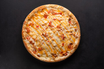 Delicious traditional homemade pizza with tomato, pepper, sausage, cheese on a black background.