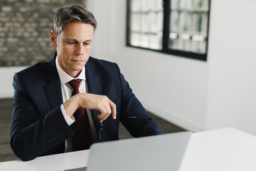 Mid adult businessman reading an e-mail on laptop in the office