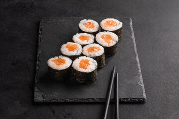 Close-up of eight sake maki rolls in plate with chopsticks on black background