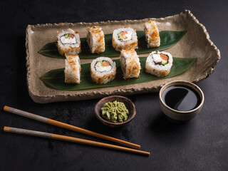 Sushi with red fish, cucumber, cream cheese on a clay plate, soy sauce, wasabi.
