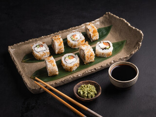 Sushi with red fish, cucumber, cream cheese on a clay plate, soy sauce, wasabi.