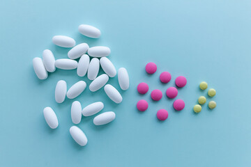 A bunch of white, pink and yellow pills on a light blue background.