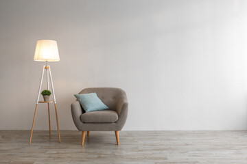 Retro armchair with blue pillow, plant in pot, glowing lamp on floor in evening