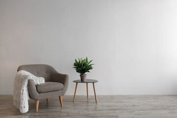 Retro comfortable armchair with soft plaid, table with plant in pot on floor on gray wall background
