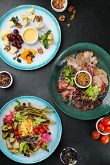 charcuterie table with three plate on dark concrete background top view. cheese plate with honey and grape, asorted pickled vegetables plate antipasti, ham plate