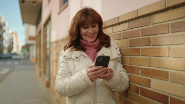 Middle age redhead woman smiling confident using smartphone at street
