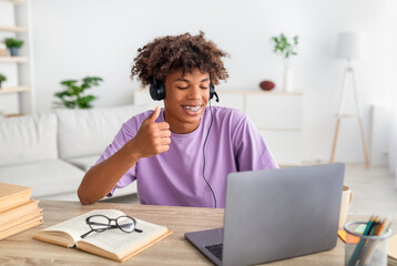Funky black teen guy wearing headphones, having online class on laptop, showing thumb up at webcam...