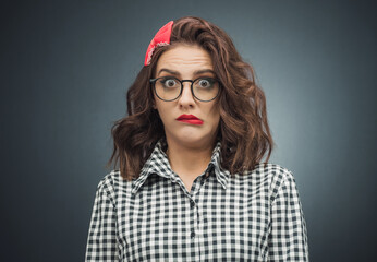 Confused young woman over dark gray - black background. A girl with funny mouth grimace.