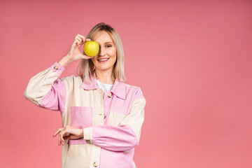 Healthy eating diet concept. Portrait of cheerful young blonde woman holding and eating green apple isolated on pink background.