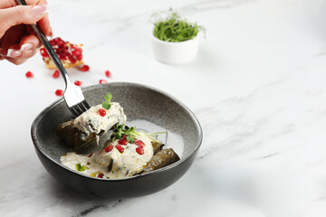 Delicious stuffed grape leaves traditional doom Mediterranean cuisine Dolma with pomegranate fruit on background. Womans hand hold fork witj dolma on light marble background.