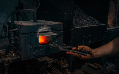 The blacksmith with tongs pulls out a red-hot blank for a knife from the forge. Furnace for heating metal.