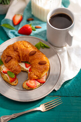 Close-up. One croissant with fresh strawberries, almond nuts, a cup of coffee. Turquoise background, white napkin. Restaurant, hotel, culinary blog, menu design.