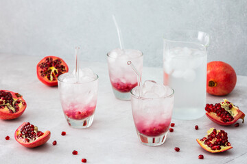 Refreshing pomegranate drink in glasses with pomegranate seeds and ice, jug of cold water with citrus, cut pomegranates with seeds