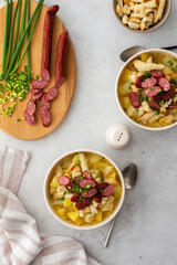 Potato and yellow pea soup with croutons and smoked meats in bowls, cutting board with chopped green onions and smoked sausage, top view