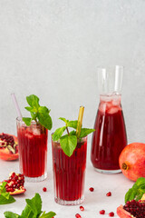 Refreshing pomegranate juice in glasses with mint and glass straw, pitcher of juice and ice, cold drink