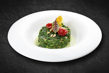 Stewed spinach with pine nuts. Isolated on a black background.