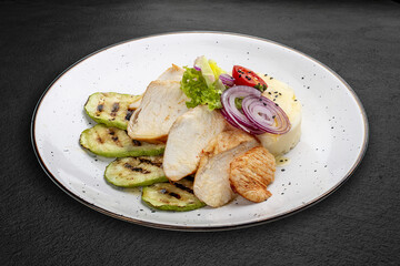 Baked chicken fillet on a pillow of mashed potatoes. Isolated on a black background.