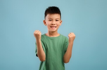 Yes. Overjoyed Little Korean Boy Shaking Fists, Celebrating Success Over Blue Background