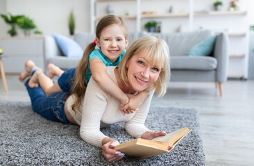 Happy mature woman and granddaughter reading book at home