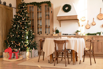 Fototapeta na wymiar kitchen decorated with pine garlands and Christmas toys. the table and near is worth Christmas tree. interior bright kitchen decorated for Christmas