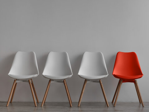 Three vacant white chairs and one red on gray wall background in office or room