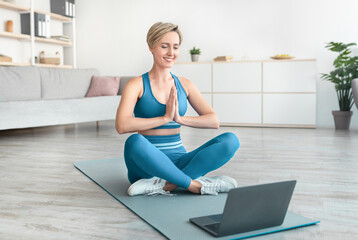 Woman meditating sitting in lotus position on mat with laptop