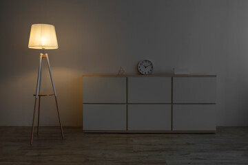 White furniture, clock, glowing lamp on floor in evening on gray wall background in office