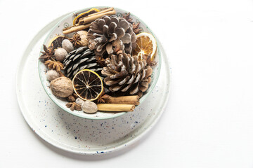 Christmas composition in a bowl. Cones, nutmeg, cinnamon, dried orange slices, anise, walnuts on a tray as home decoration for the New Year on the white wooden table