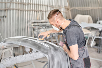 Small Garage. The mechanic works with a grinding tool. Sanding of car elements. Painting car service. Repairing car section after the accident.