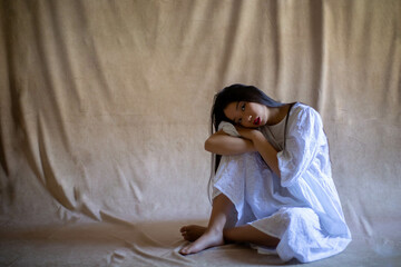 Bella chica asiática con camisón sentada en el suelo sobre fondo ámbar