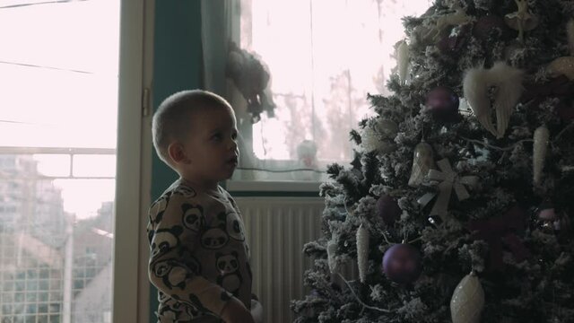 Cute little 4 years old boy standing and looking  at Christmas tree at home
