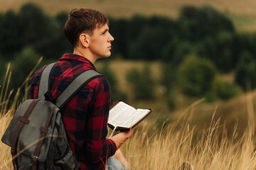 Reading the Bible outdoors in nature. A man in sunglasses and a shlap holds a Bible in his hands