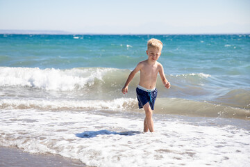 Fototapeta premium Cute little boy playing on the beach by the sea, he is happy. Concept summer vacation, rest, fun.