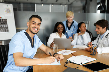 Handsome doc smiling at camera while having brainstorming with colleagues