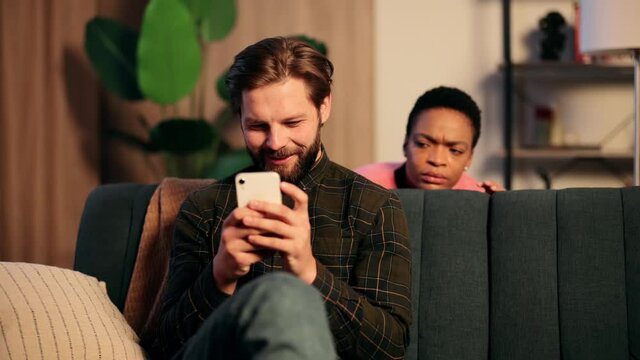 Jealous girlfriend trying to read messages on the mobile phone of her boyfriend while he is not watching. Interracial couple. High quality 4k footage