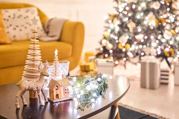 Decorated table in the Christmas interior. Christmas tree. Close-up a small house, Cones, garland, and other Christmas tree toys. light from the garlands
