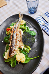 Roasted pike perch or cod fish with baked vegetables and spinach. Dish decorated with a slice of lemon. Restaurant menu