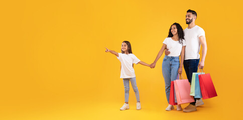 Arabic Family Shopping Holding Bags Pointing Finger Aside, Yellow Background