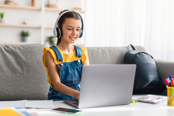 Girl sitting on couch using laptop, wearing headset