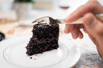 Closeup macro of fork cutting dark French death by chocolate layered dark cake slice on white plate...
