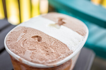 Closeup macro of container carton tub of dark and milk chocolate vanilla neapolitan ice cream frozen dessert gelato storebought with texture of dairy cream three flavors
