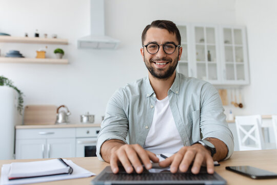 Cheerful mature caucasian male with beard in glasses typing on keyboard, work on laptop, look at webcam