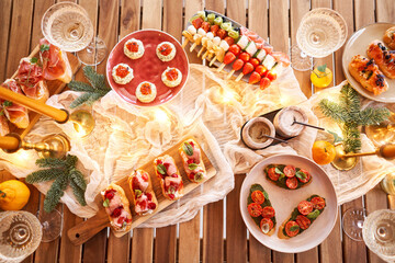 Christmas dinner feast. A small table is served with snacks, bruschettas, and canapes. A decorated dining table with champagne glasses, candles and christmas tree an garland in background