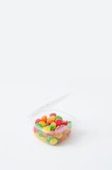 Delicious sweets in the plastic box on a white background. Sugar candies in red, green, yellow, orange and purple. A modern concept of sweets.