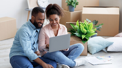 Smiling millennial african american wife showing to husband laptop with new room design, sitting on...